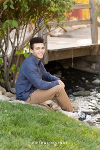 young adult wearing blue and khaki poses near a creek for some fall family portraits in Reno