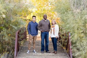 family of three in fall clothing stand on a cool bridge in northwest Reno for Reno fall family portraits
