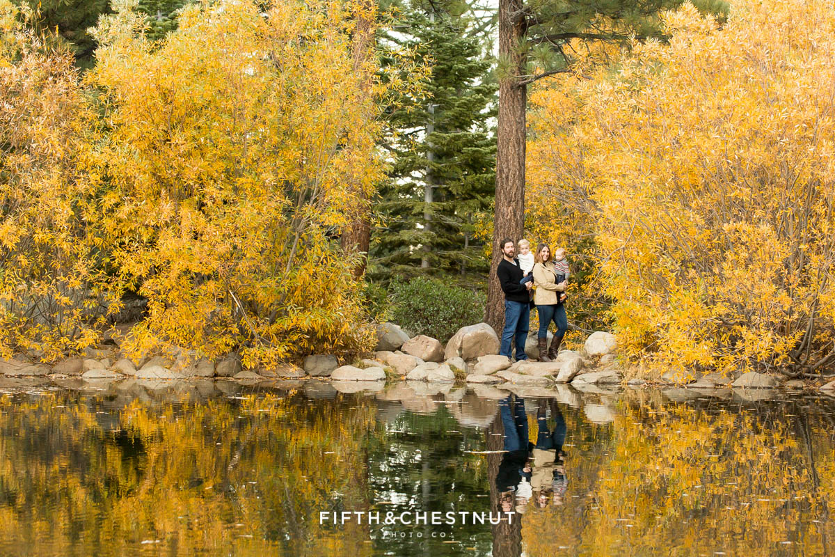 Family of four standing near pond showing their reflection among yellow trees for their Fall Galena Creek Portraits