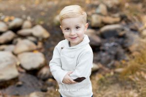 A toddler smiles near a creek during his family's galena creek portraits by Reno Family Photographer