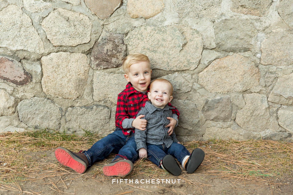 young brothers sit together against a stone wall for their reno family photos at galena creek park