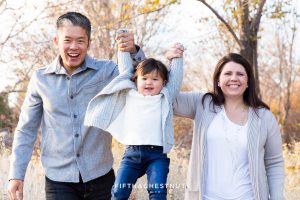 Mom and Dad swing 2 year old daughter in the air by her hands to make her laugh for Adorable Reno Family Portraits