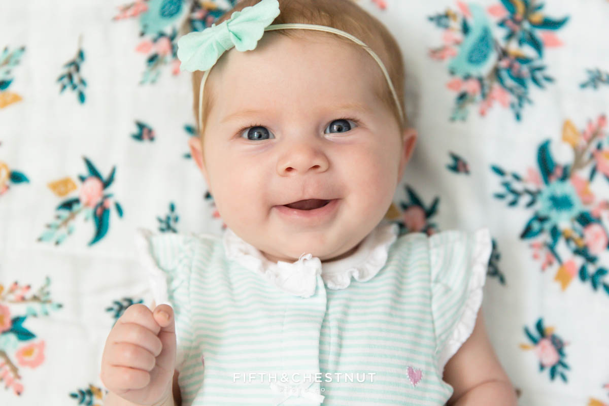 3 month old baby girl smiling at Reno Baby Photographer on a teal, pink and white muslin meadowlark blanket background
