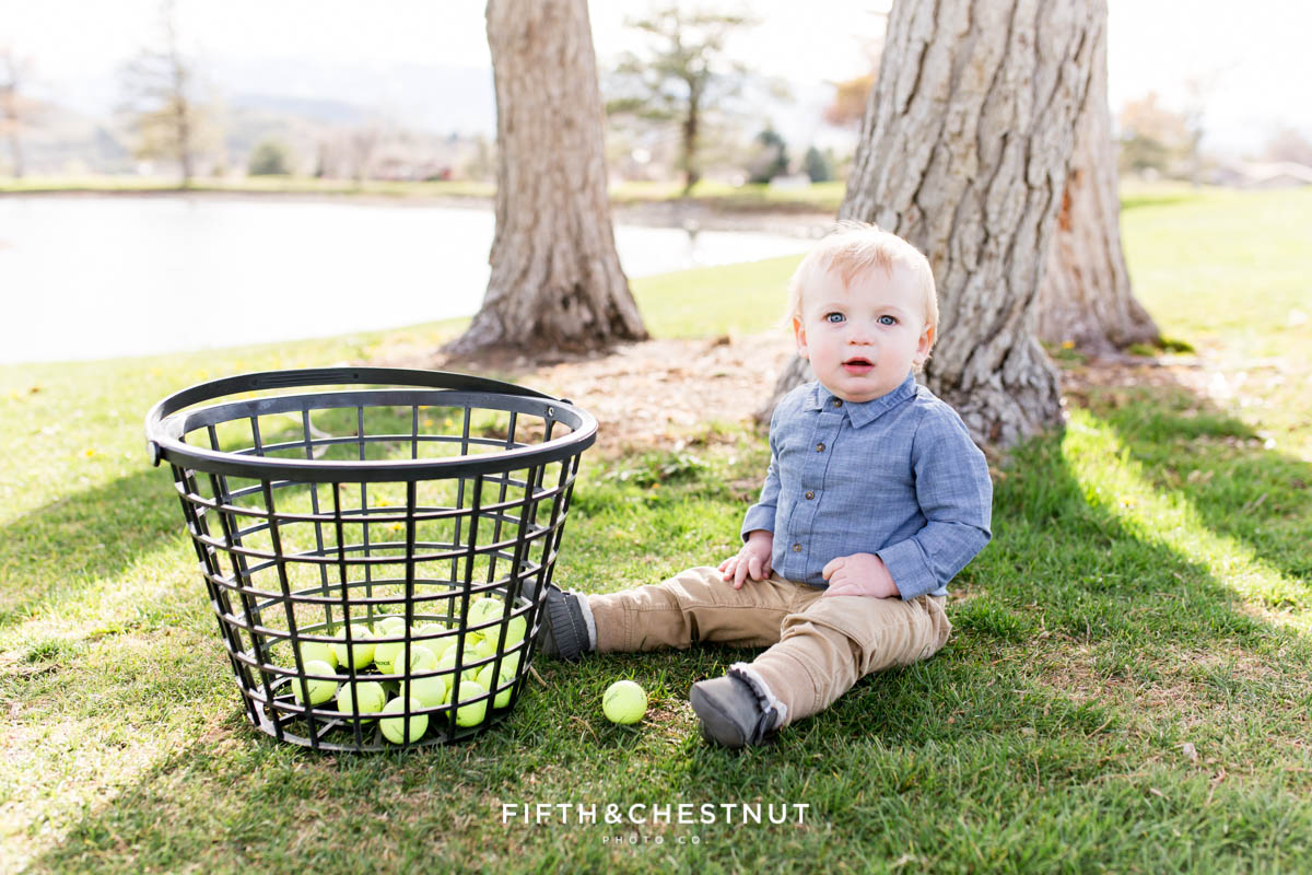 Baby boy posing with toy golf clubs and a basket of golf balls at Hidden Valley Country Club for his Golf Themed One Year Photos by Reno Baby Photographer