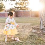 sweet Reno 2 year portraits of a little girl playing with pine needles in the park while wearing a yellow floral dress
