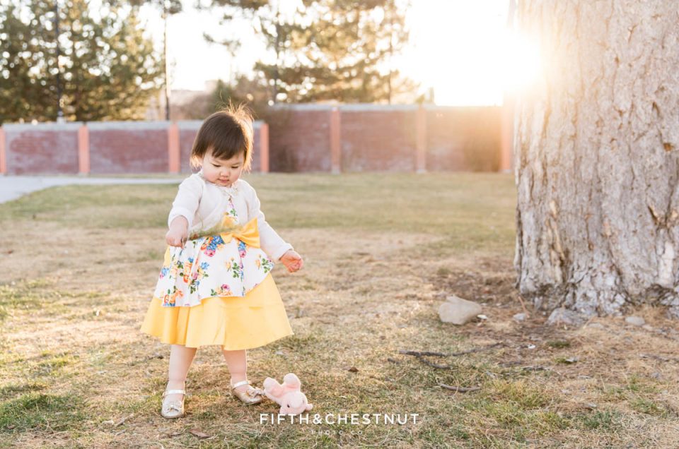 sweet Reno 2 year portraits of a little girl playing with pine needles in the park while wearing a yellow floral dress