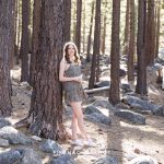 a reno high school senior leans against a tree in the woods for her forest high school senior portraits