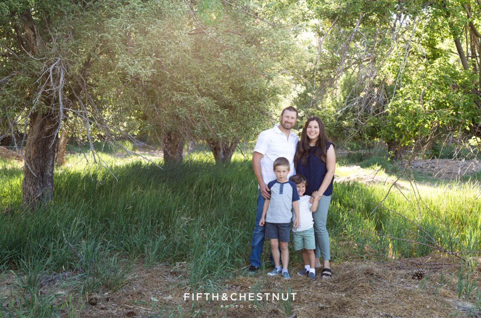 A family of four stands amidst tall grasses and apple trees in a meadow for their Spring Verdi Family Photos
