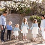 a family of six wearing neutral and pastel colors holds hands and smiles for their bright and airy family portraits