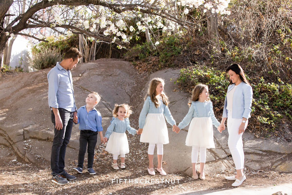 a family of six wearing neutral and pastel colors holds hands and smiles for their bright and airy family portraits