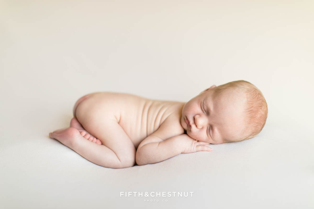 a beautiful baby boy on a neutral blanket sleeps peacefully during his newborn twin photos by Reno Family Photographer