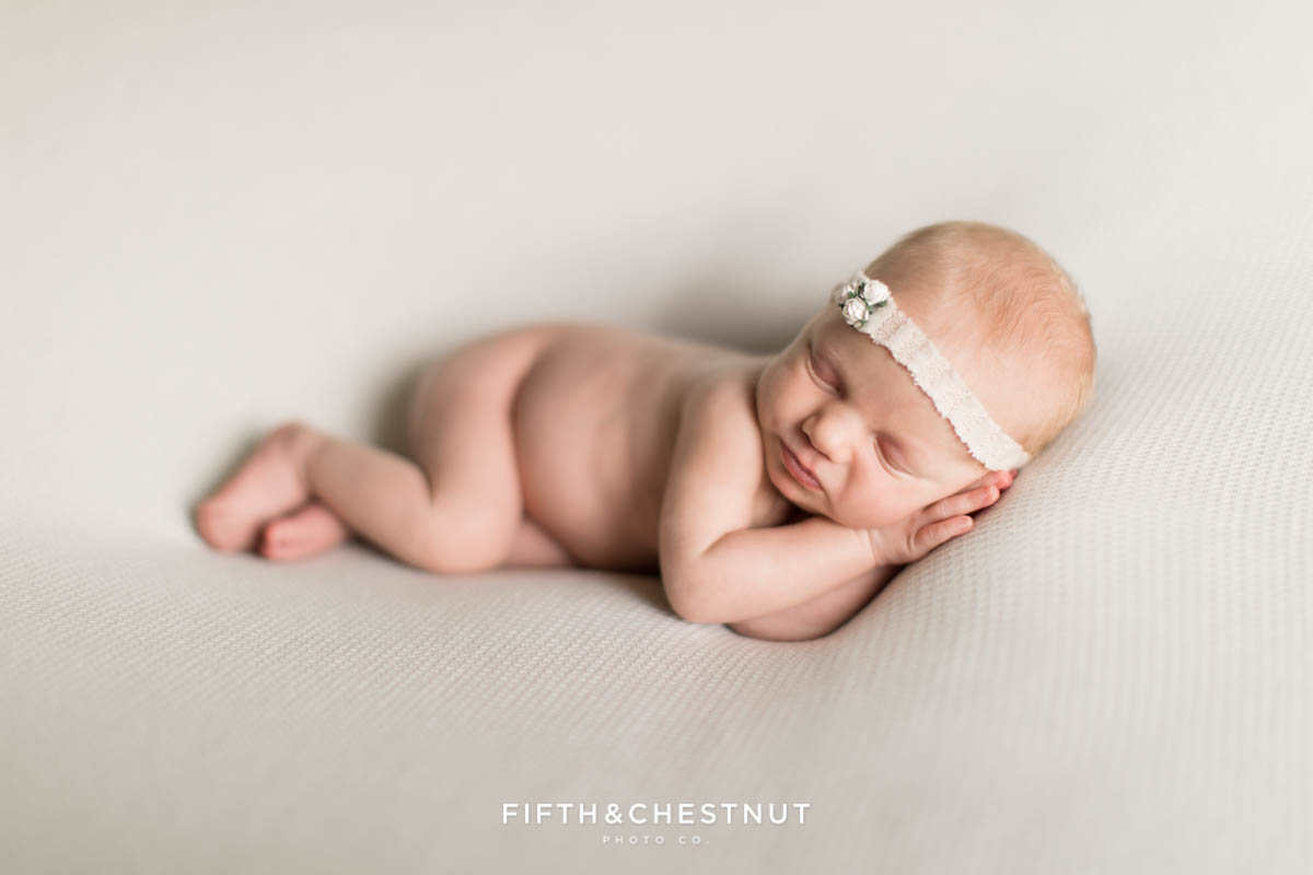 A baby girl lays with sleepy hands under her face for her neutral newborn twin photos by Reno Family Photographer