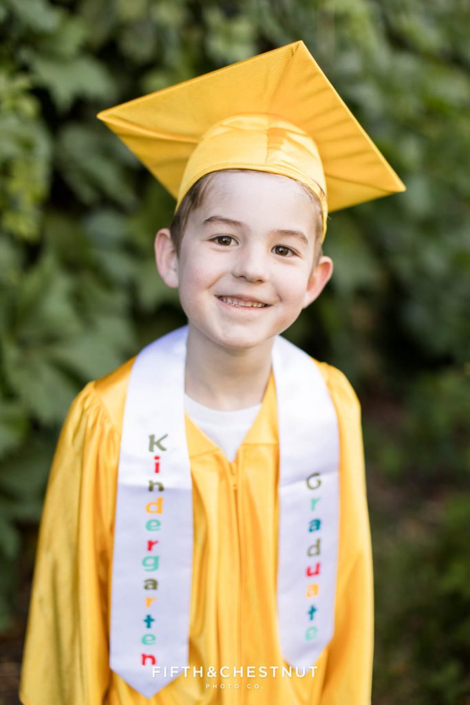 Kindergarten Cap and Gown Portraits of a young boy wearing a gold gown, gold cap and a white sash that says "kindergarten graduate" in front of an ivy wall at UNR in late spring