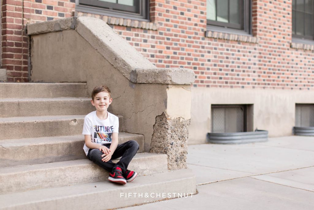 A young boy sits on steps to an old building at UNR for his kindergarten graduate pictures