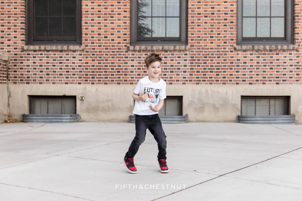 A young boy jumping in front of a brick building at UNR for his Reno child Portraits