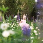 A sweet three year old girl in a pink dress twirls around a patch of lupines and daisies for spring wildflower portraits by reno child photographer