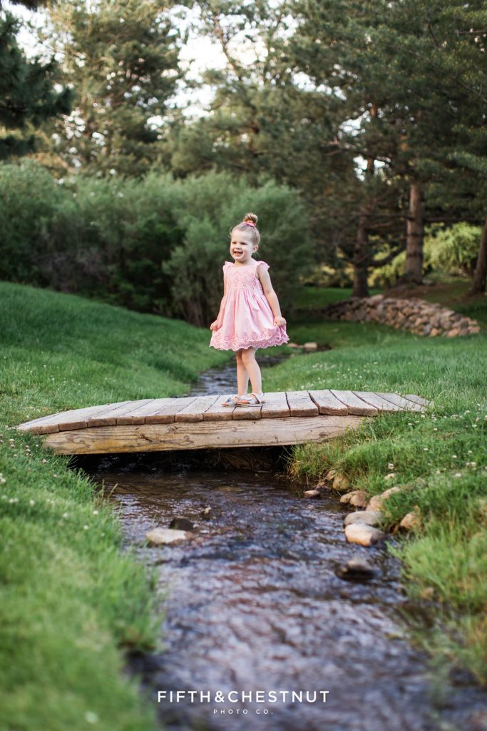A Girl stands on a bridge over water for her Purple & Pink Spring wildflower child portraits by Reno Child Photographer