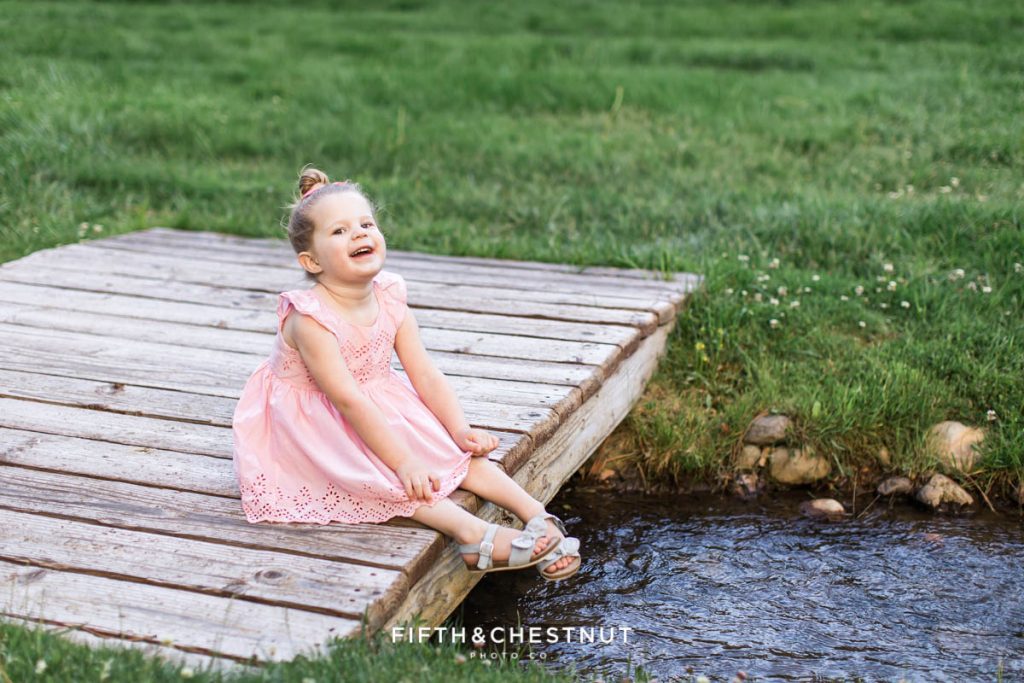 A little girl sits on a little wooden bridge over a small creek in reno for spring wildflower portraits by reno child photographer