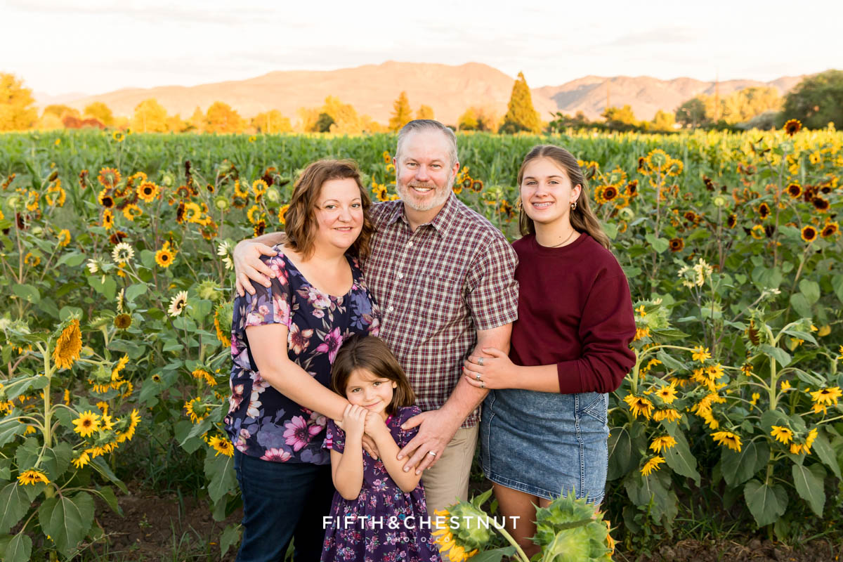 A family of four with a sunflower field all around them with the sunlit mountains in the background for their sunflower family photos in Reno, NV.