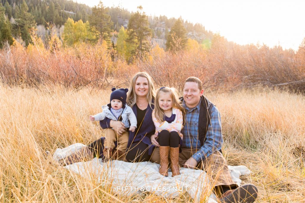 A cute family of four sits on a fuzzy fur blanket in Hope Valley for their gorgeous and cozy Hope Valley family portraits