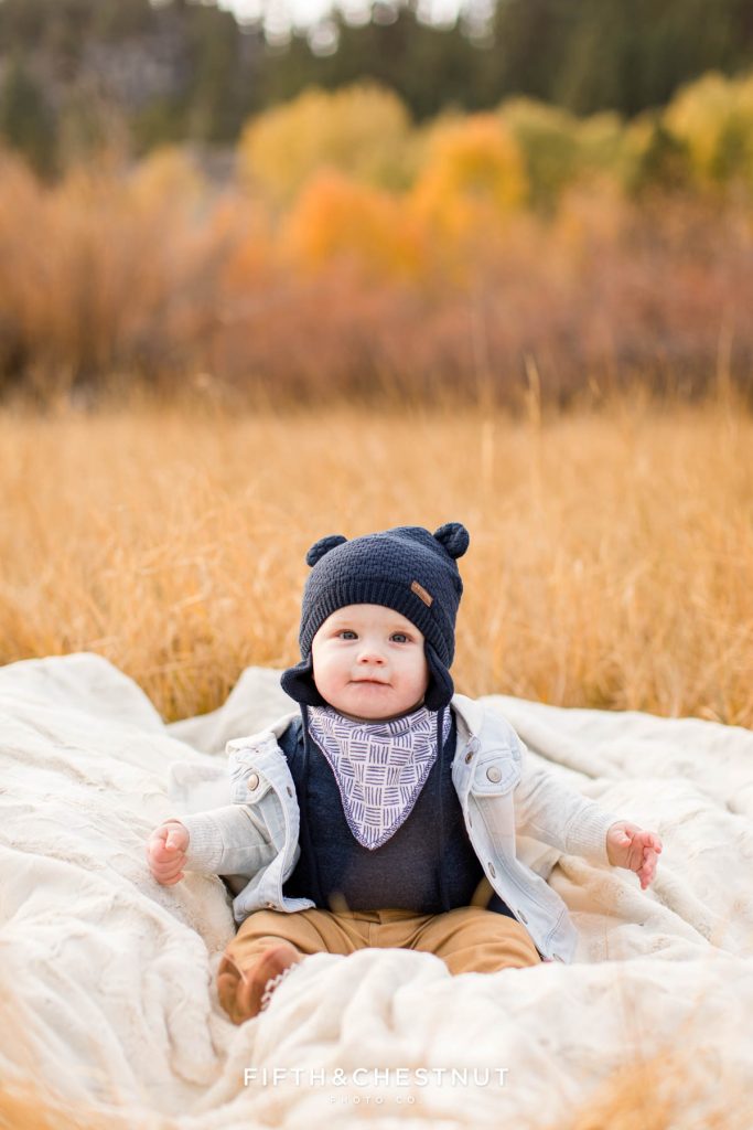 a baby sits on a fuzzy blanket and smiles for his Hope Valley family portraits in October