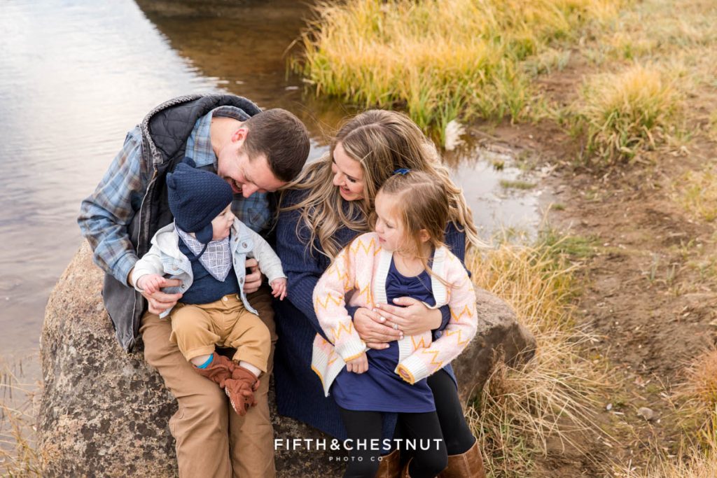 A family cuddles and laughs together on a big rock by the river for their Hope Valley family portraits