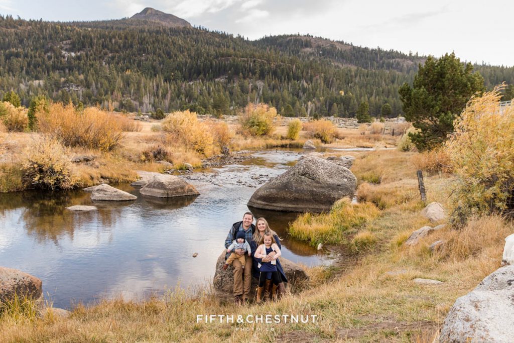 a gorgeous mountainous landscape sits behind a family of four as they sit on a rock for their Hope Valley family portraits