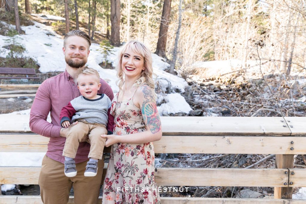 A family of three huddles together on a wooden bridge for their winter Reno family portraits at Galena Creek Park