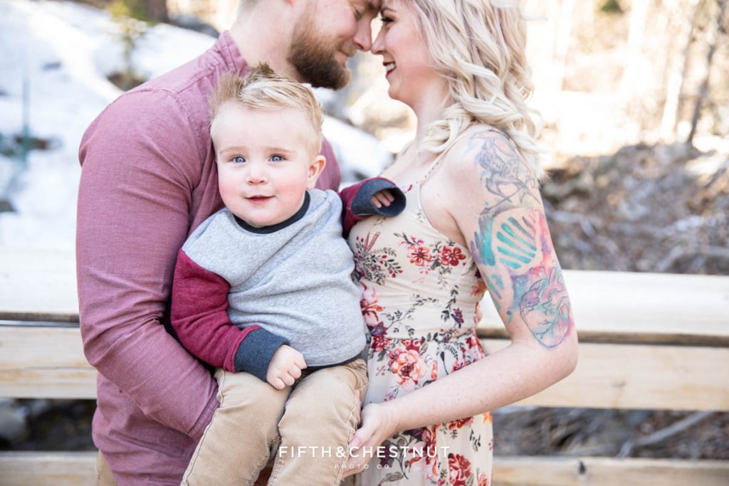 A little boy smiles while his mom and dad look into each other's eyes in the background for winter Reno family portraits by Reno family photographer