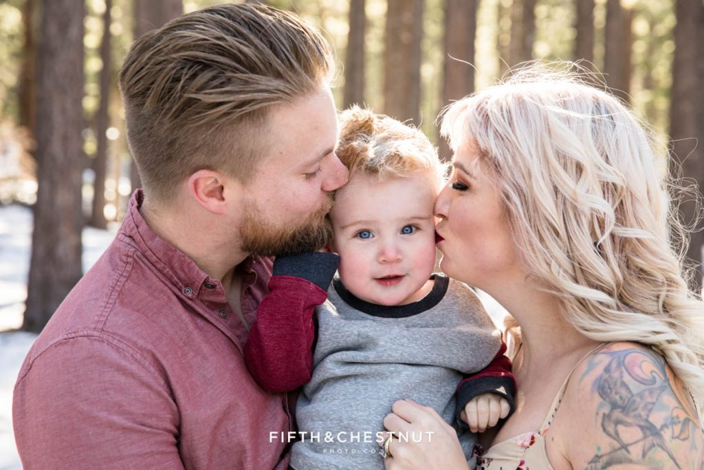 a toddler's face is squished by his mom and dad's kisses during their winter Reno family portraits at Galena Creek Park