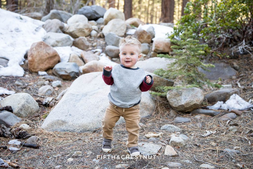 A toddler walks towards the camera with rocks behind him for his winter Reno family portraits by reno family photographer
