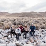 A family gathers on rocks with a vast desert background behind them for desert family portraits by Reno Family Photographer