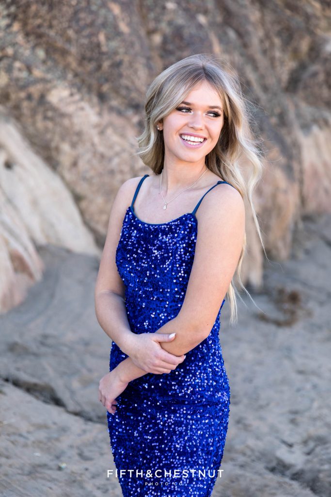 A high school student in a blue sequin prom dress shows off her professional hair and makeup for reno senior portraits by Reno senior photographer at Moon Rocks in Nevada