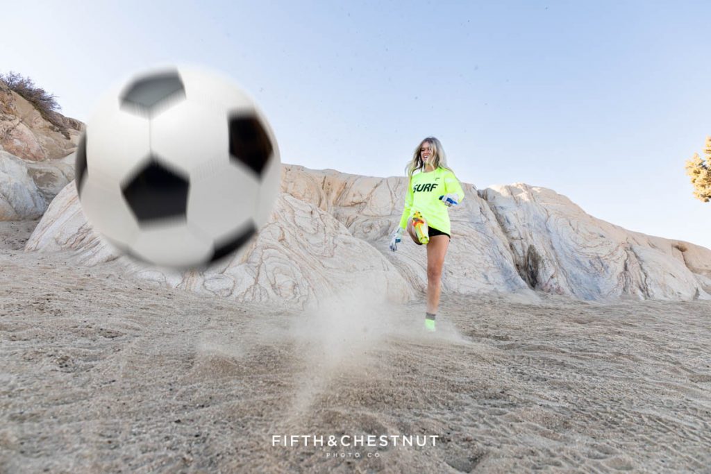 A soccer themed portrait of a Reno high school senior wearing Neon yellow and kicking a soccer ball directly at the Reno Senior Photographer