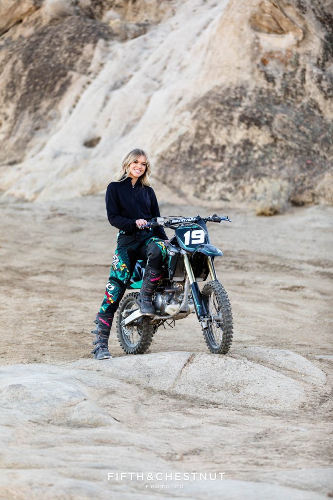 Senior standing against her dirt bike at Moon Rocks in Reno, NV for her senior portraits
