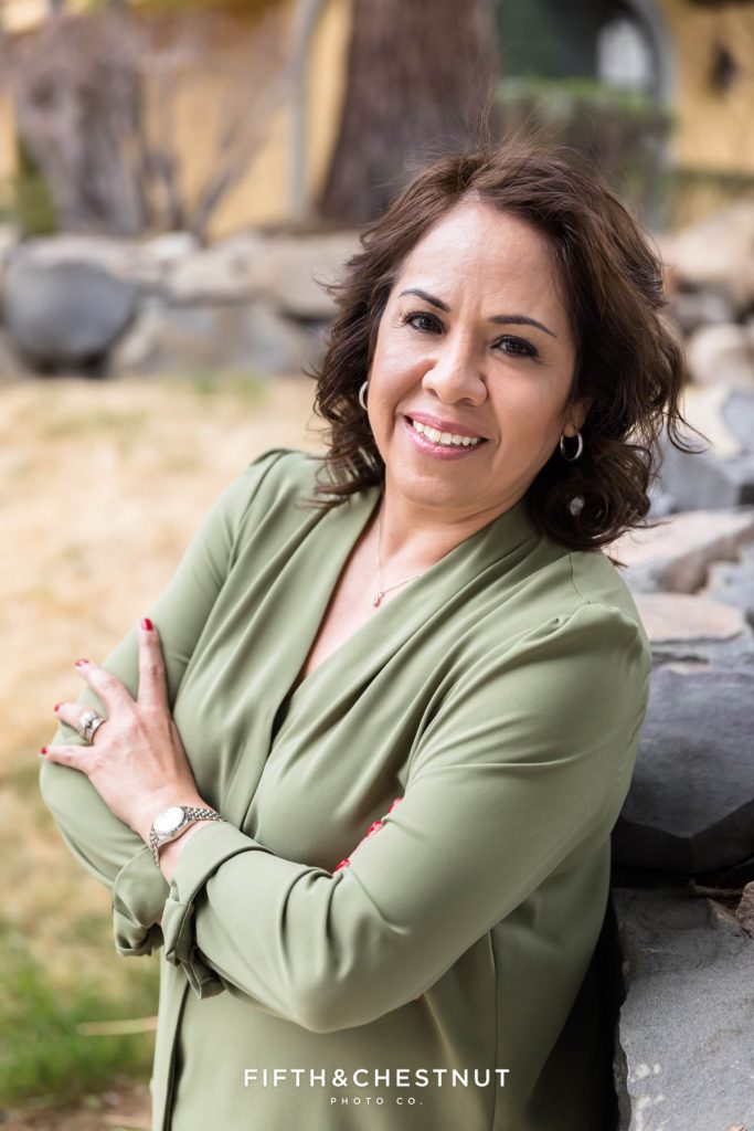 A woman with dark hair and a green blouse crossing her arms and leaning on a rock retaining wall for her early Spring Reno Headshots