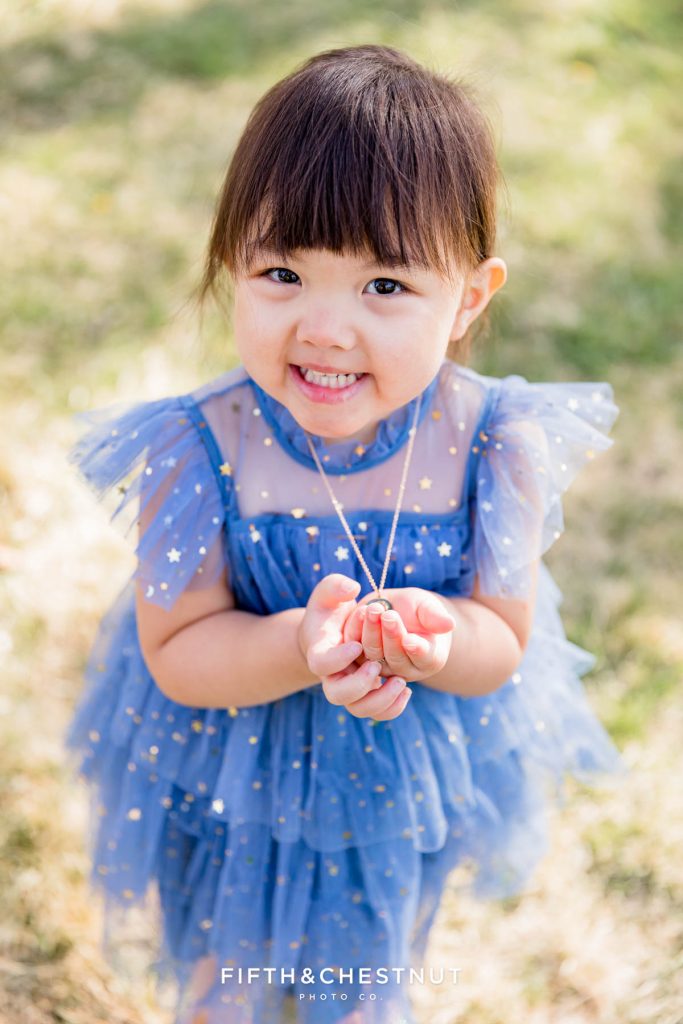 Springtime family Portraits in Reno by Reno Family Photographer of little girl holding her necklace while wearing a baby blue dress with gold stars with grass in the background