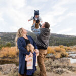 A dad holds his 6 month old son in the air while his wife and daughter look at them lovingly for reno family portraits by Reno Family Photographer