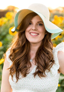 Redheaded Reno Photographer wearing a sun hat with mint green accents and a floral boho style dress in a field of sunflowers