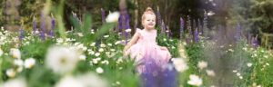 A 3-year-old girl wearing a fancy pink princess dress dances in the purple and white wildflowers in Reno for her Reno child portraits with Reno Family Photographer on a beautiful spring day