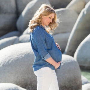 A pregnant woman wearing a denim shirt and white skinny jeans poses in front of the boulders at Sand Harbor for her Reno maternity portraits by Reno Family Photographer