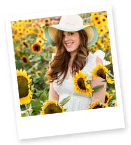 A polaroid image of a redheaded photographer wearing a mint green sun hat and a white boho style dress with intricate floral details and ruffled shoulders in a field of blooming sunflowers