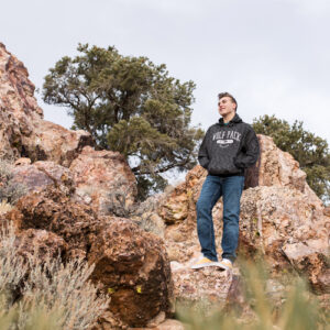 A Damonte Ranch High School Senior student wearing a UNR Wolf Pack sweatshirt while standing on red rocks on Geiger Grade in Reno for his Reno senior photos by Reno High School Senior Photographer