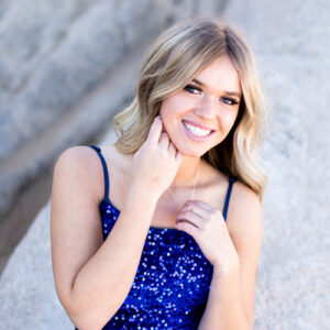 A Damonte Ranch High School Senior wearing a royal blue sequin dress smiles and plays with her necklace for her Reno Senior Portraits at Moon Rocks by Reno Senior Photographer