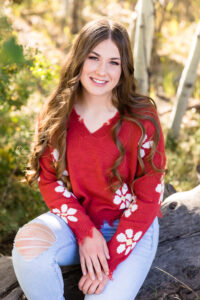 A Reno High School senior student relaxes on a wooden log in the forest for her Reno Senior Portraits by Reno Senior Photographer on a sunny Autumn day wearing red, white and denim.