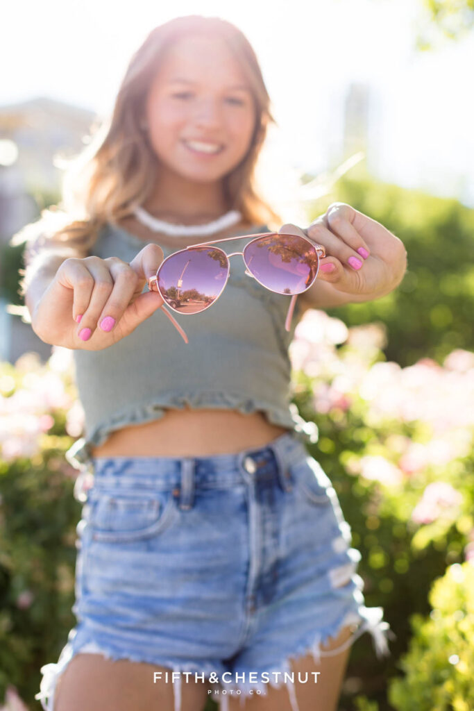 Teen girl hold out aviator sunglasses in an example of why summer is the best season for senior portraits in Reno/Tahoe.