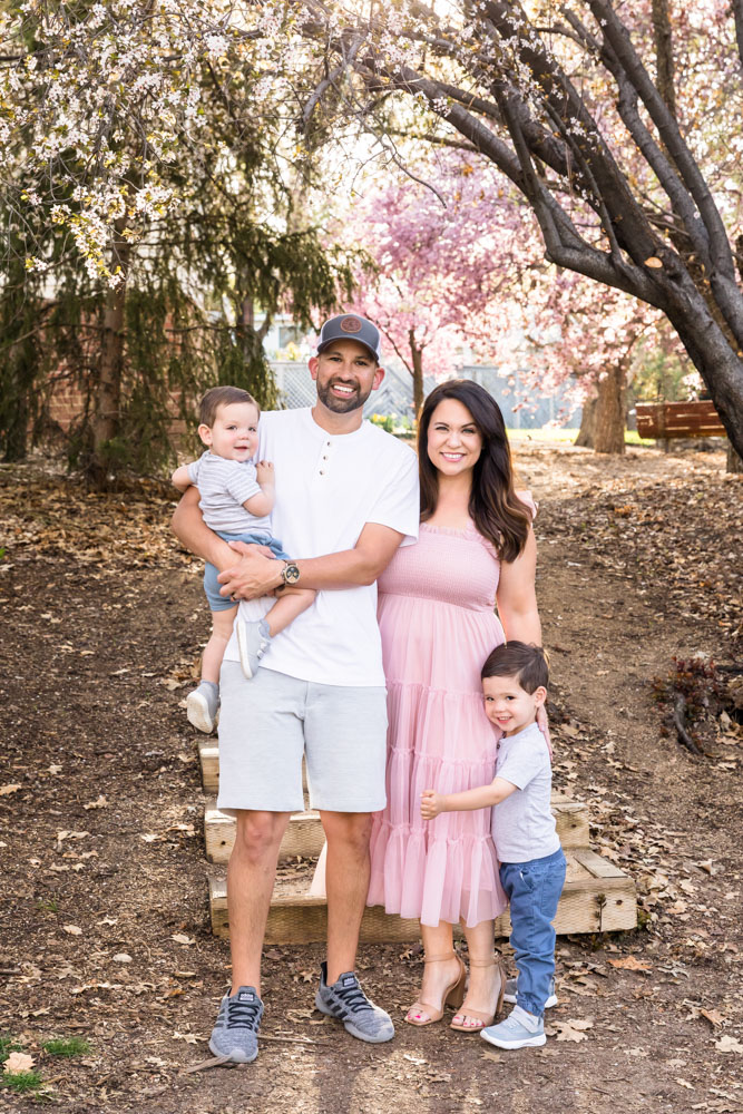Precious spring family photos in Reno at Rancho San Rafael with smiling kids and parents with blooming plum trees in the background.