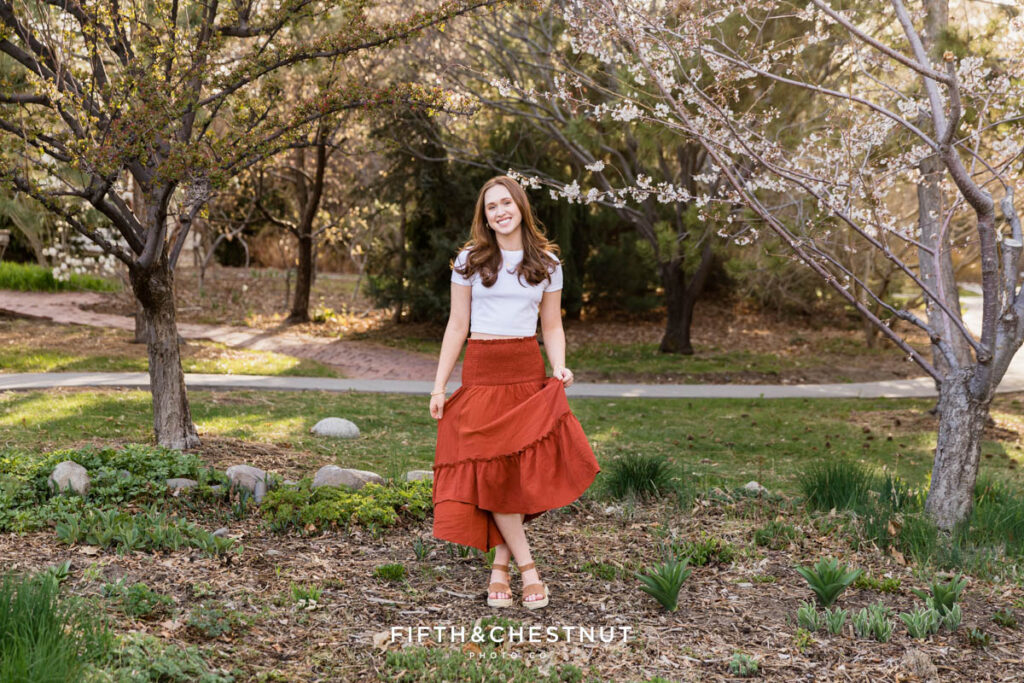 Stunning spring boho Reno senior portraits at Rancho San Rafael by Reno Senior Photographer with Ava with blooming pear and plum trees in the background.