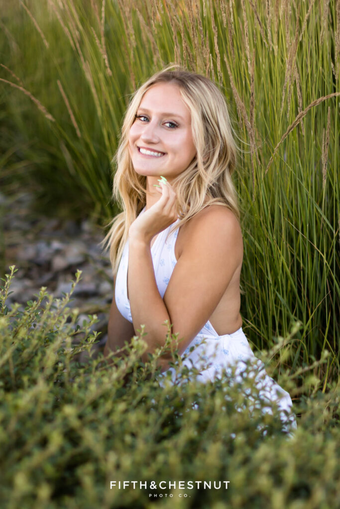 Stunning and sunny summer Reno Senior Photos of Rylan at sunset in front of tall green grass while wearing a white and blue mini dress.