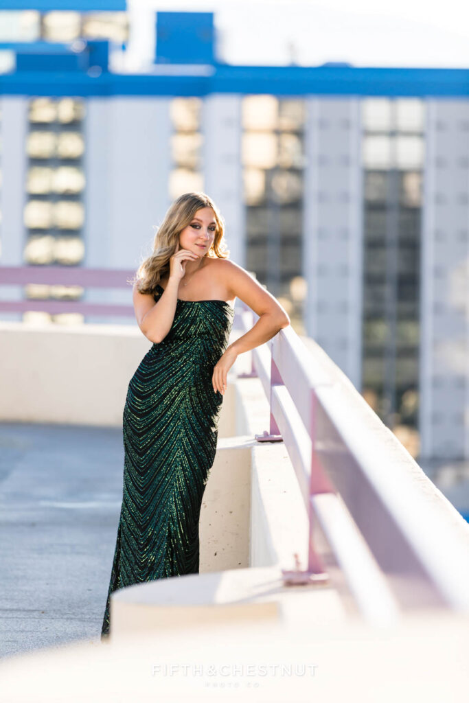 Edgy and modern senior portraits of a female senior wearing an elegant and sparkly prom dress set against the backdrop of a casino with reflective windows.